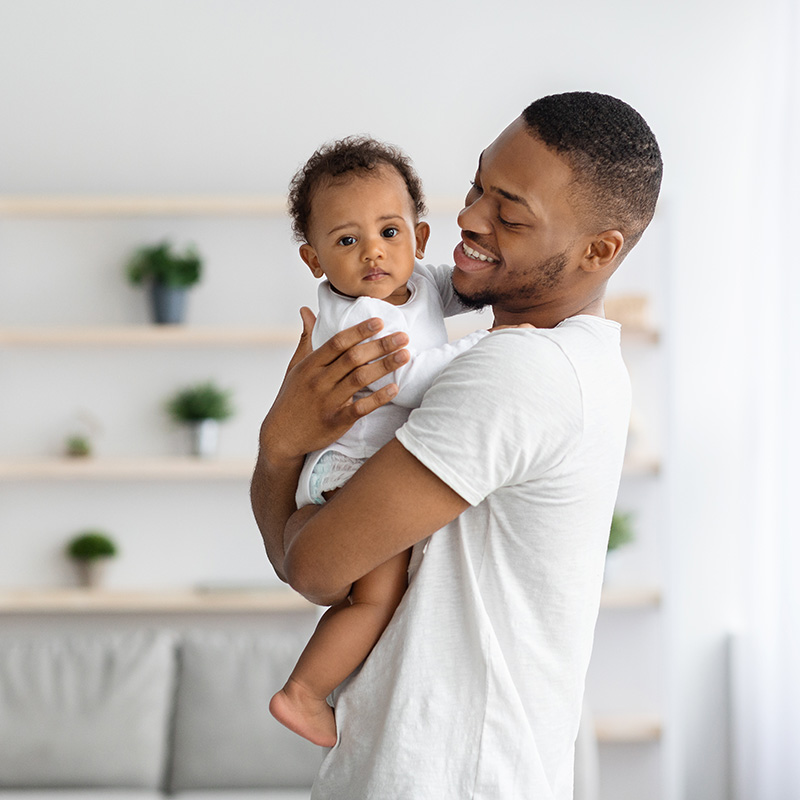 young black father holding a baby in living room, wearing white
